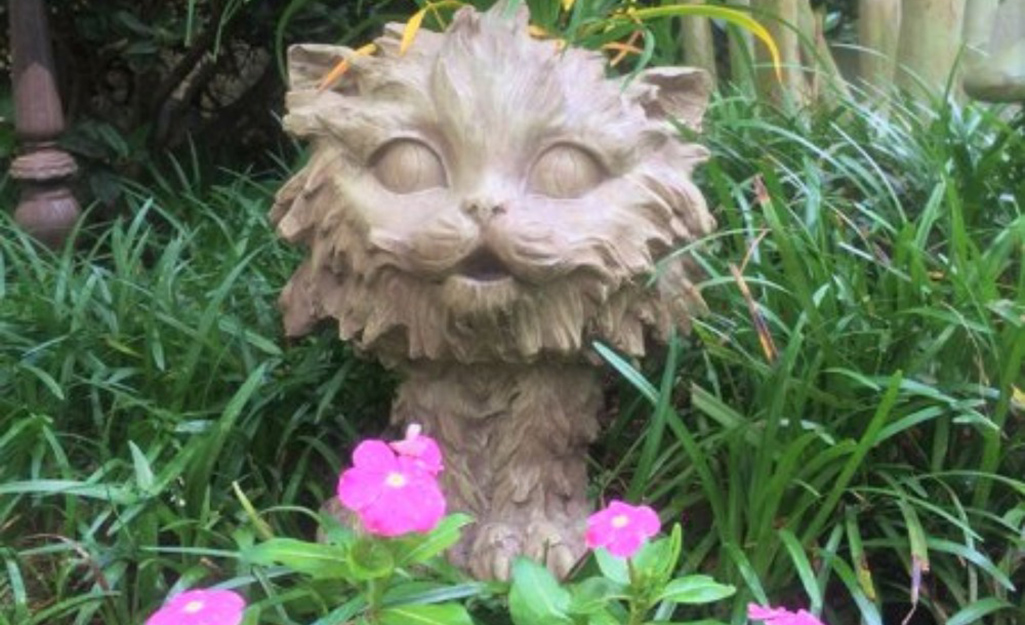 A kitty statue beside flowers in a garden bed.