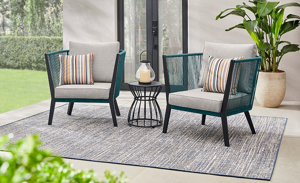 Outdoor chairs, table and lantern on a patterned outdoor rug. 