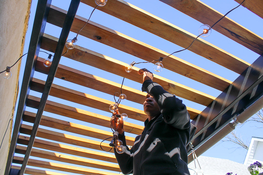 A person hangs string lights from the ceiling of a balcony.