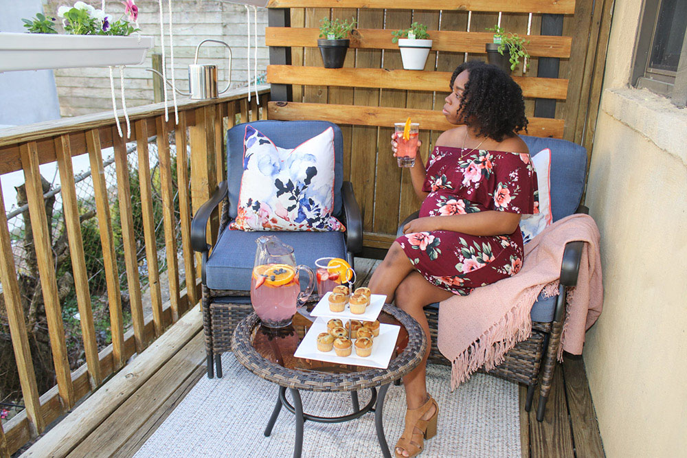 A woman holds a drink while looking over her patio balcony.
