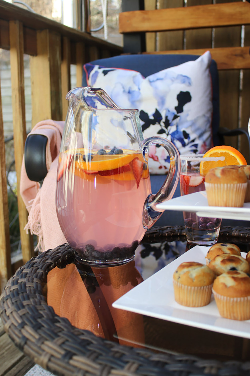 A patio table decorated with a pitcher of drinks and a tray of mini muffins.