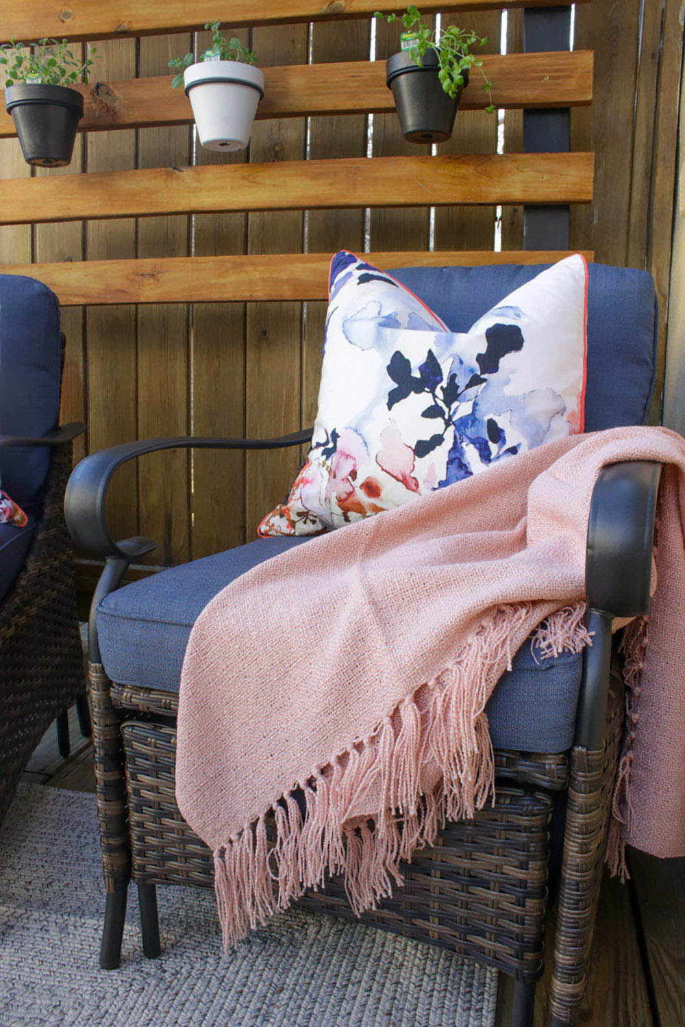 An outdoor patio chair decorated with a pink throw and a pillow.