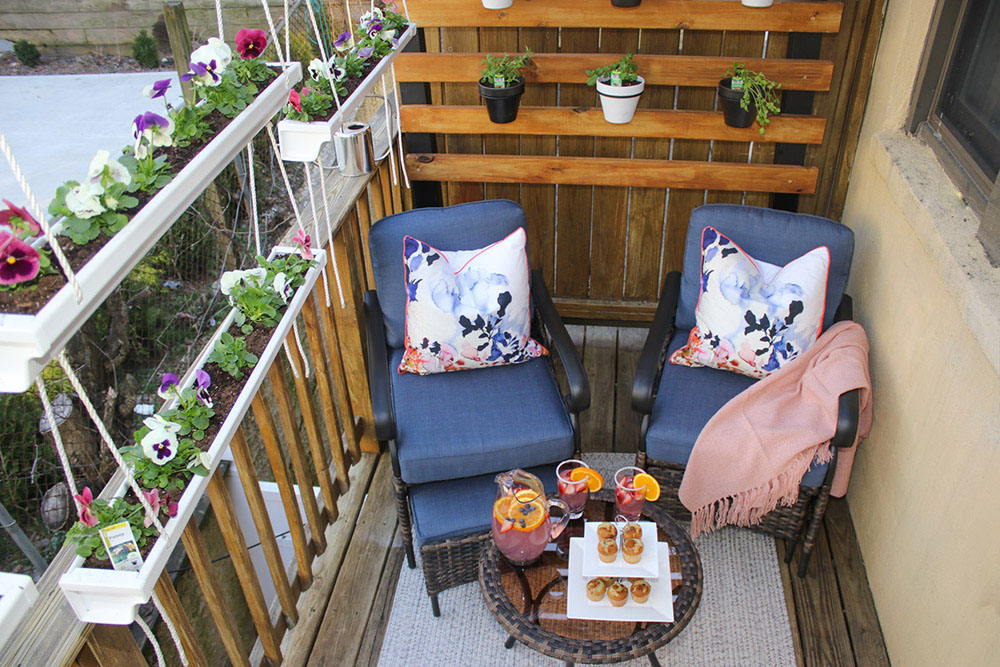 A small balcony area decorated with a two patio chairs, a small table, and flowers.