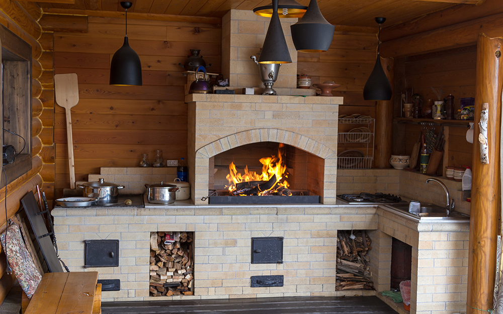 A brick fireplace with a wood fire and kitchen amenities built in.