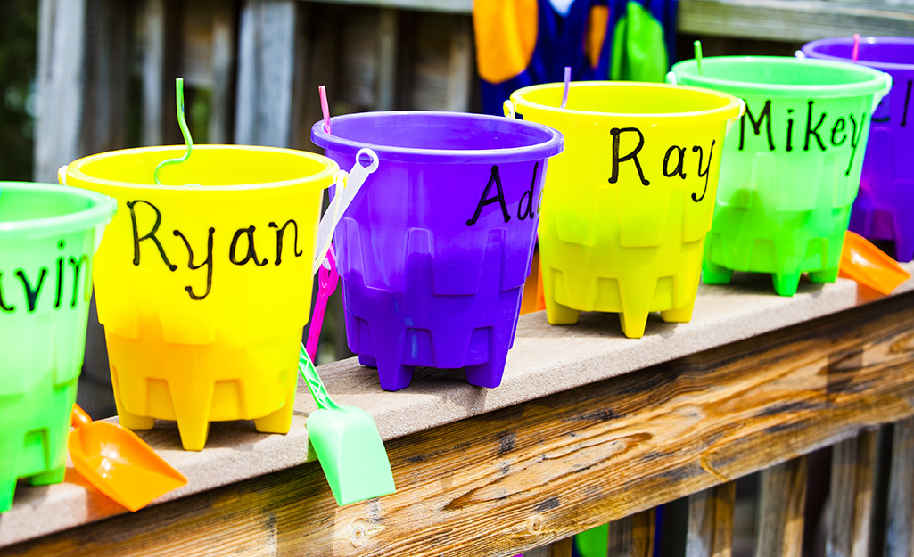 Beach buckets with names on them sit on a railing.