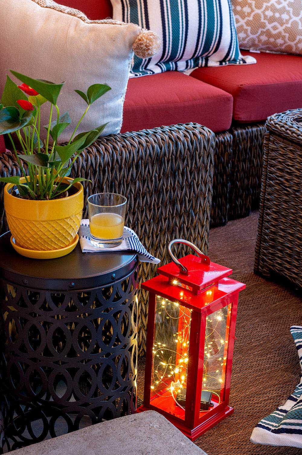 A red lantern filled with string lights sits next to a black garden stool with a yellow planter.