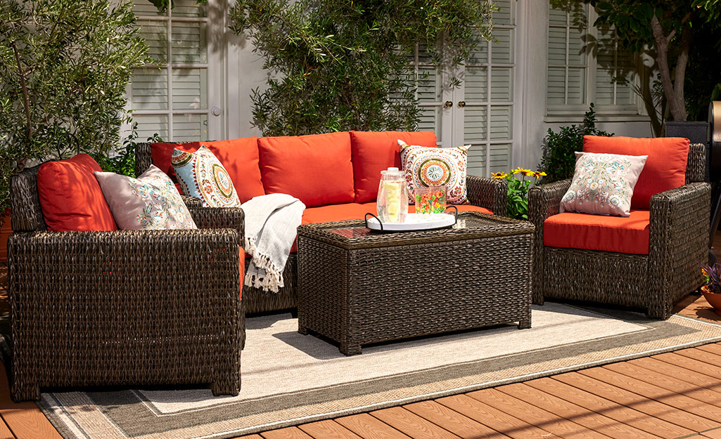 Throw pillows complement the orange cushions of a wicker patio set with a sofa, two chairs and a matching coffee table.