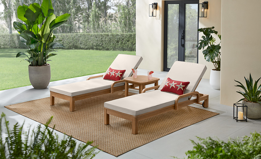 Red pillows depicting starfish accent two minimalist lounge chairs sitting side by side on an outdoor rug on a patio.