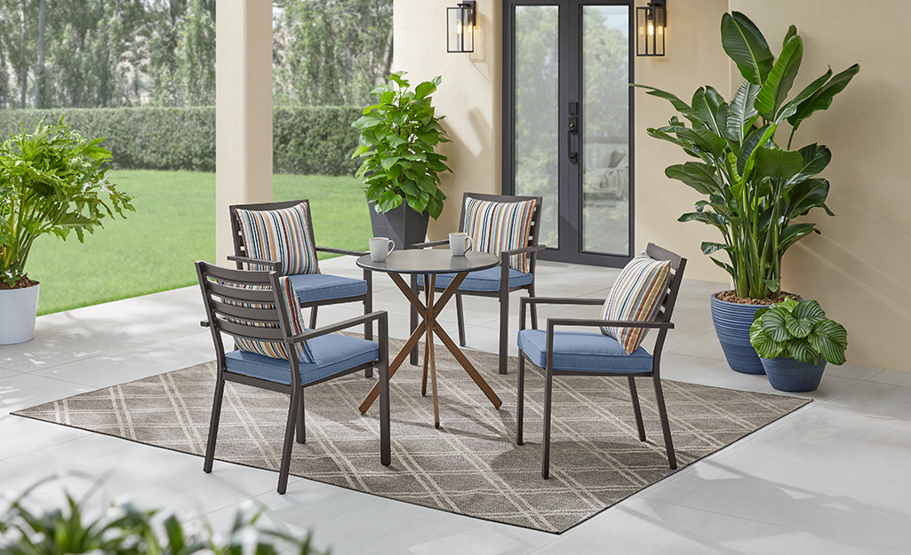 Tall potted plants accent a patio with four dining chairs with blue cushions and a round table.