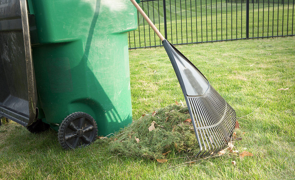 A lawn rake resting on a garbage can.