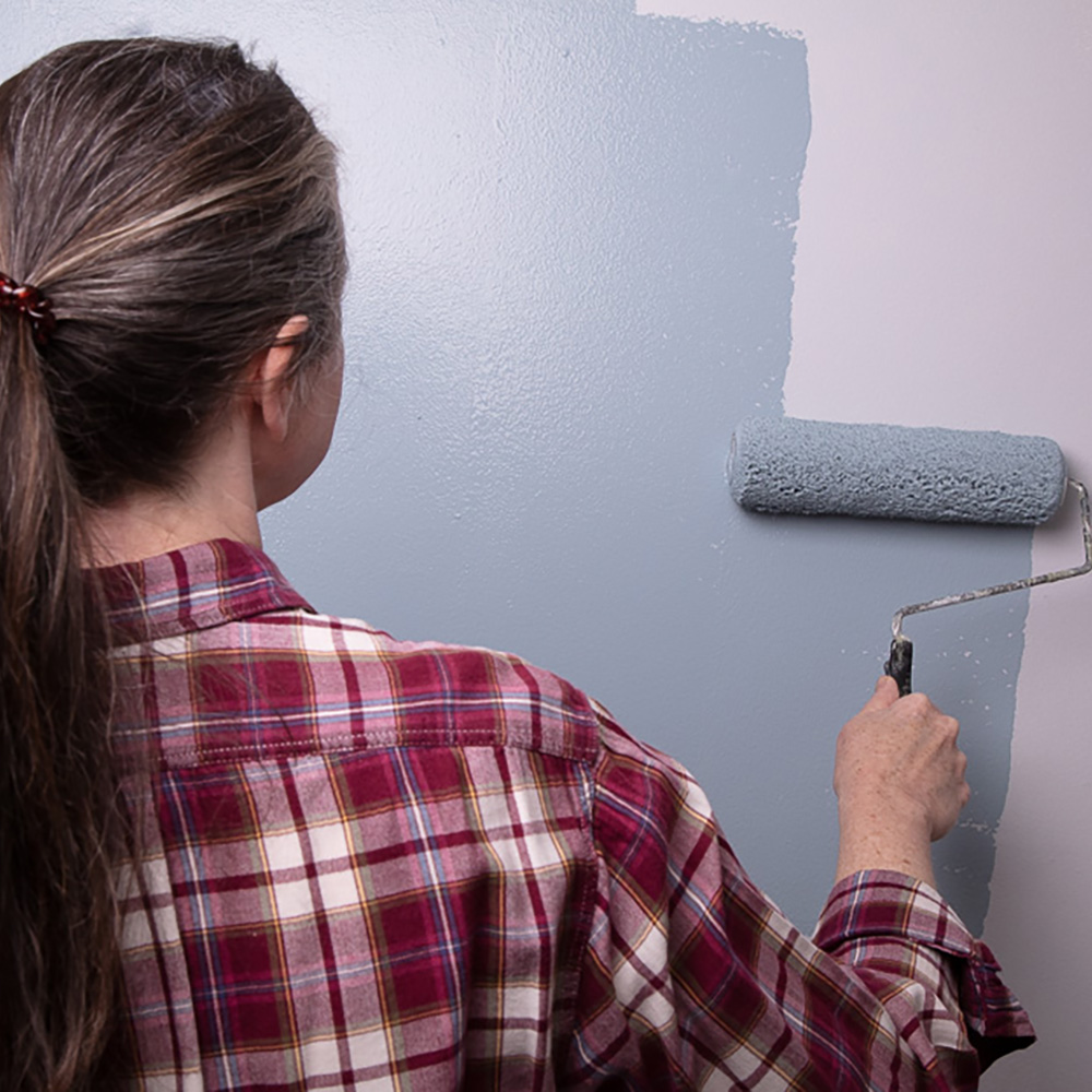 Woman using a paint roller to paint a wall.