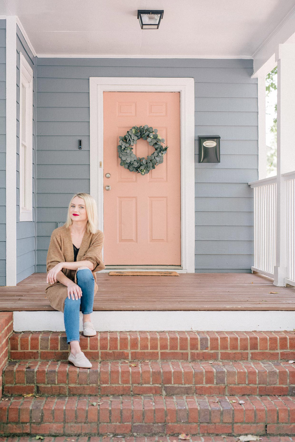 A woman sitting on a front porch in front of a pink door.