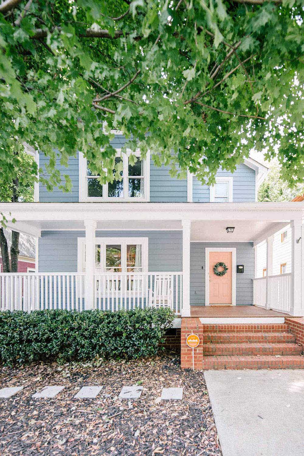 The front of a home with a blue exterior, white trim, and a pink door with a wreath.