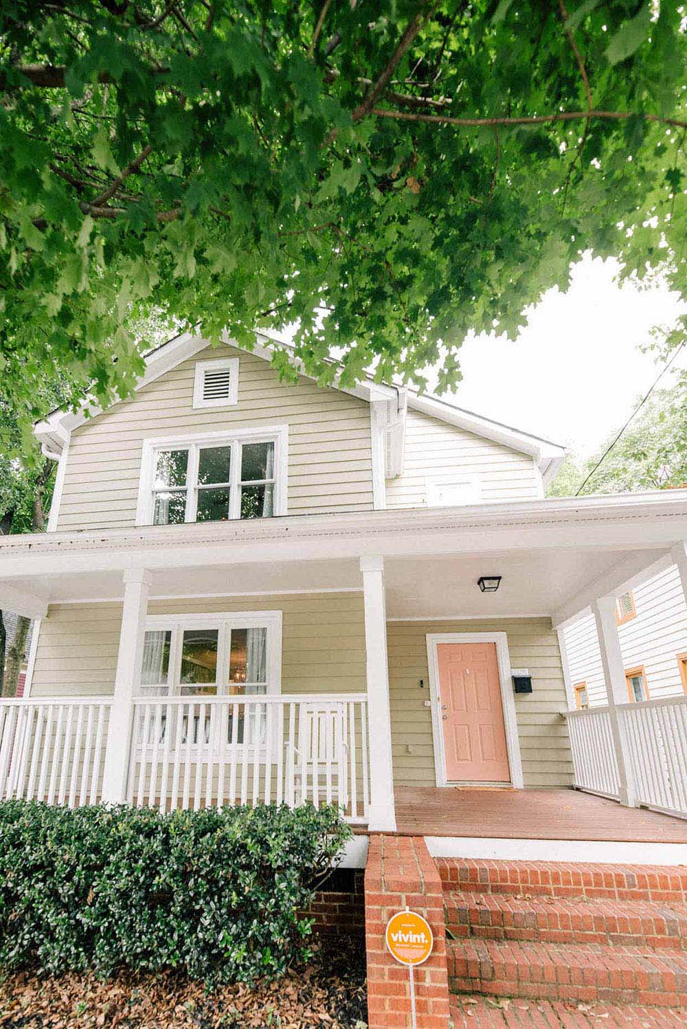 A beige home with white trim and a pink door.