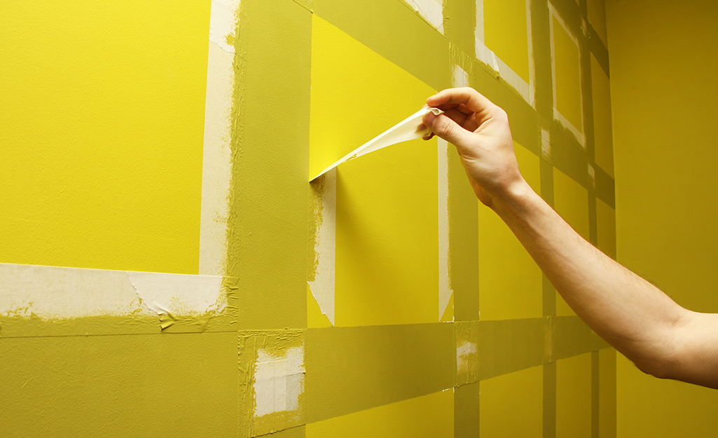 A person removing tape from a recently painted wall.