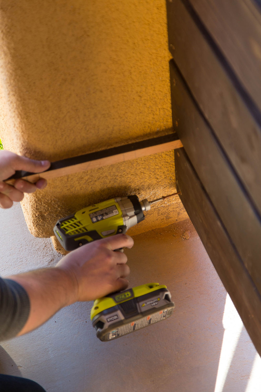 A man using a Ryobi drill to attach planks of wood to an outdoor wall.