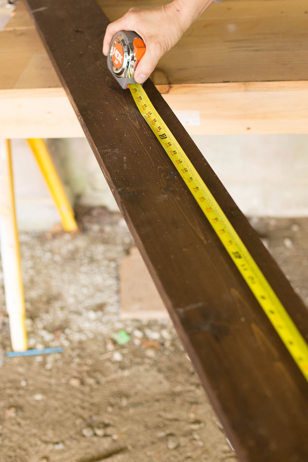 A man measuring a piece of lumber with measuring tape.