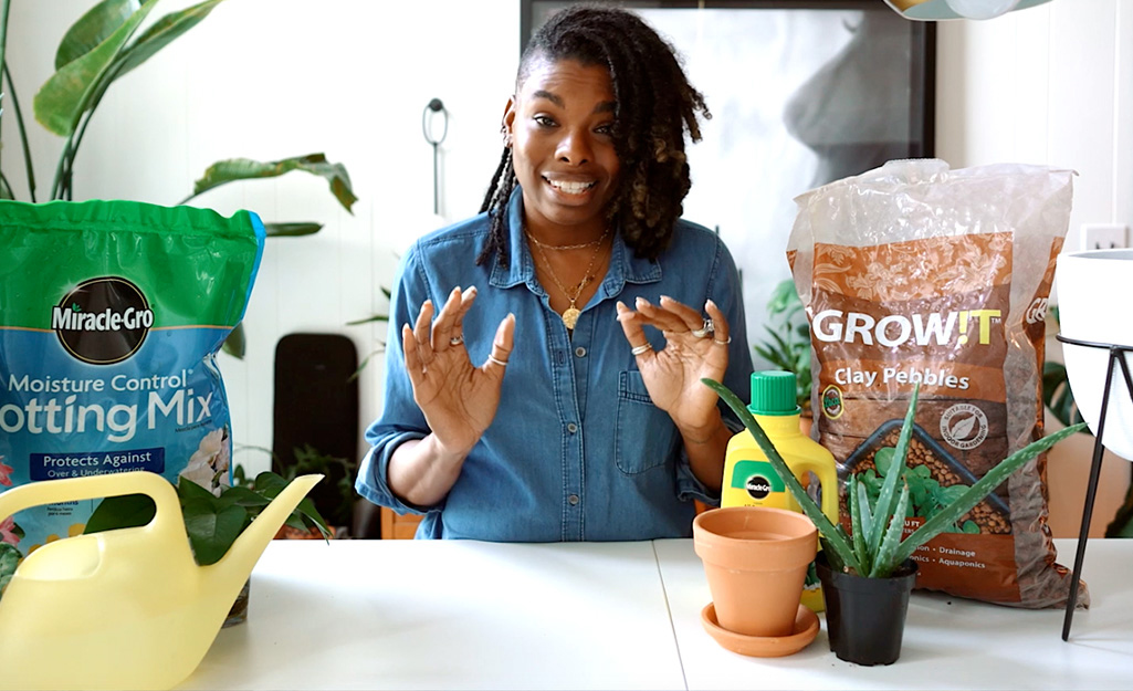Woman sitting at a table with potting mix, planters and house plants.