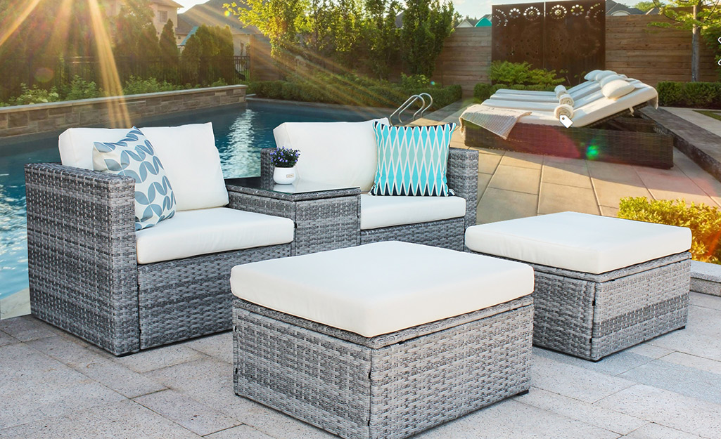 A gray wicker poolside lounge set with cushions and ottomans.