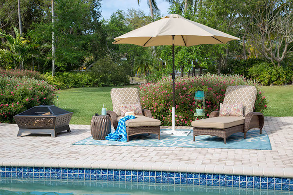 A pool patio decorated with chaise lounge chairs and a fire pit.