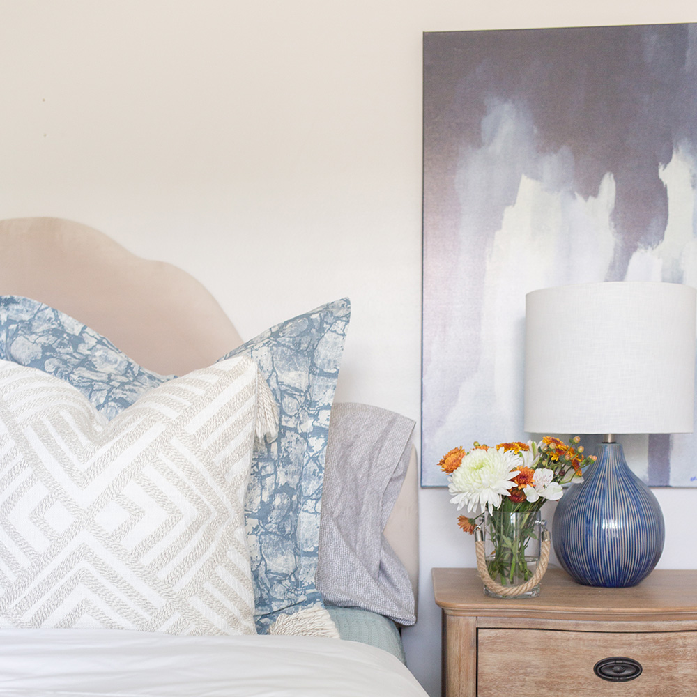 A guest room with a wooden nightstand and blue decorative lamp.