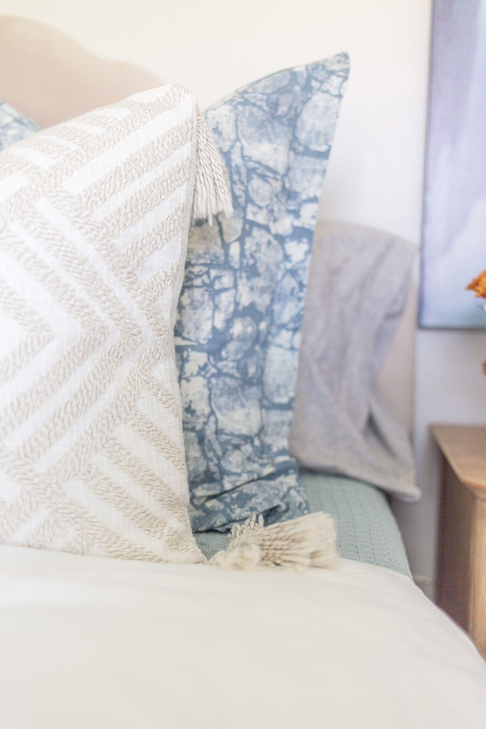 A white and natural geometric embroidered throw pillow sitting in front of a blue euro sham.