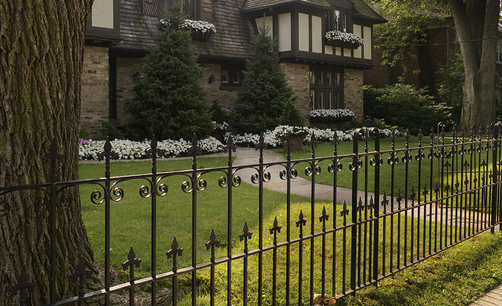 An ornamental metal fence stands in front of a Tudor-style home