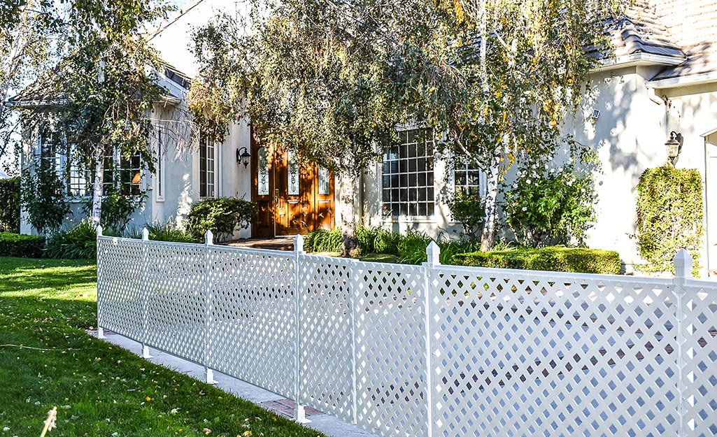 A white lattice fence stands in front of a house with large windows and an ornate front door