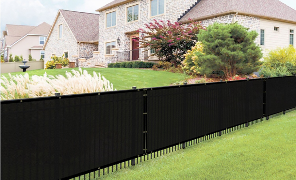 A black mesh privacy screen is attached to a black fence that divides two yards