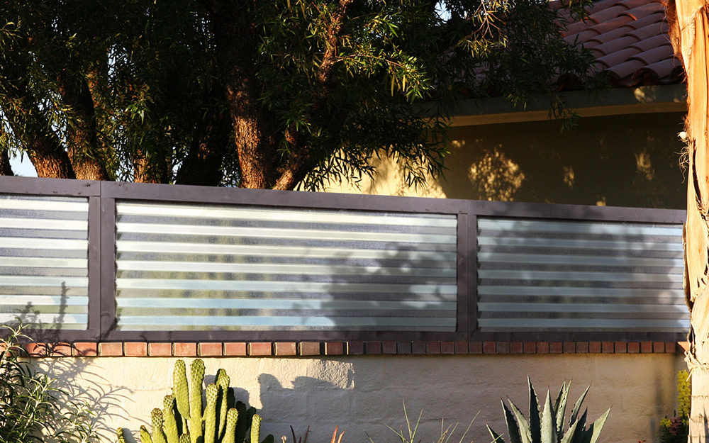 Corrugated metal privacy fencing atop a wall.