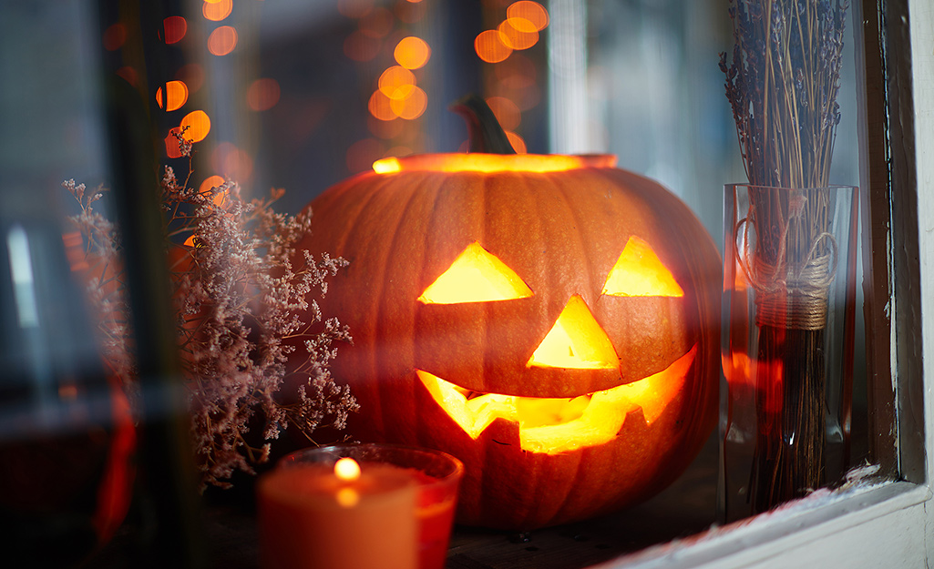 A glowing Jack-o'-lantern next to a candle in a window.