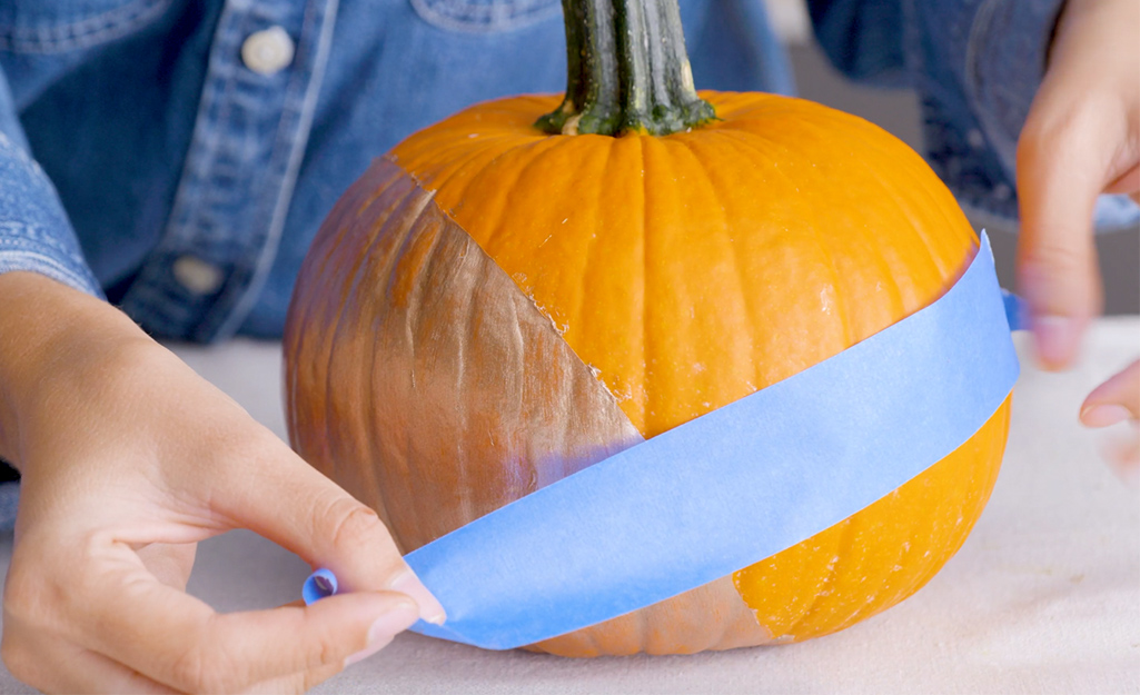 A person placing painter's tape on a pumpkin.
