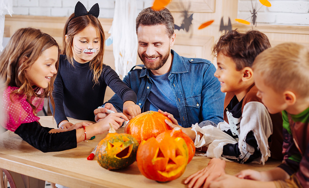 A person helping a group of children decorate pumpkins.