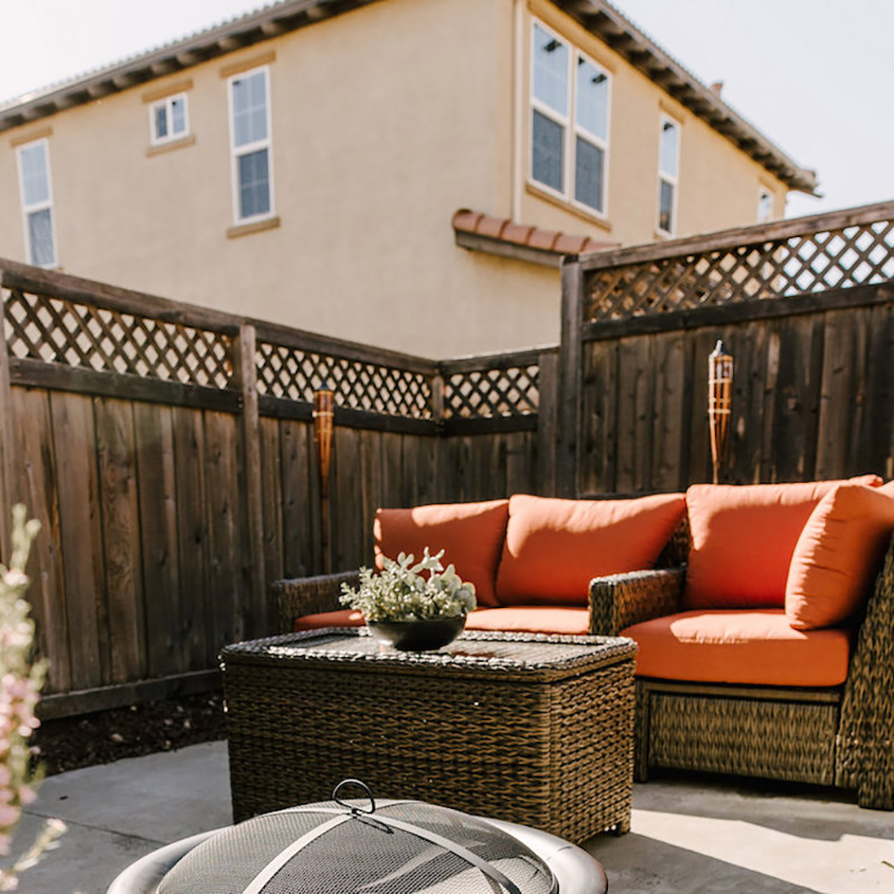 A patio with wicker furniture surrounded by a wood fence.