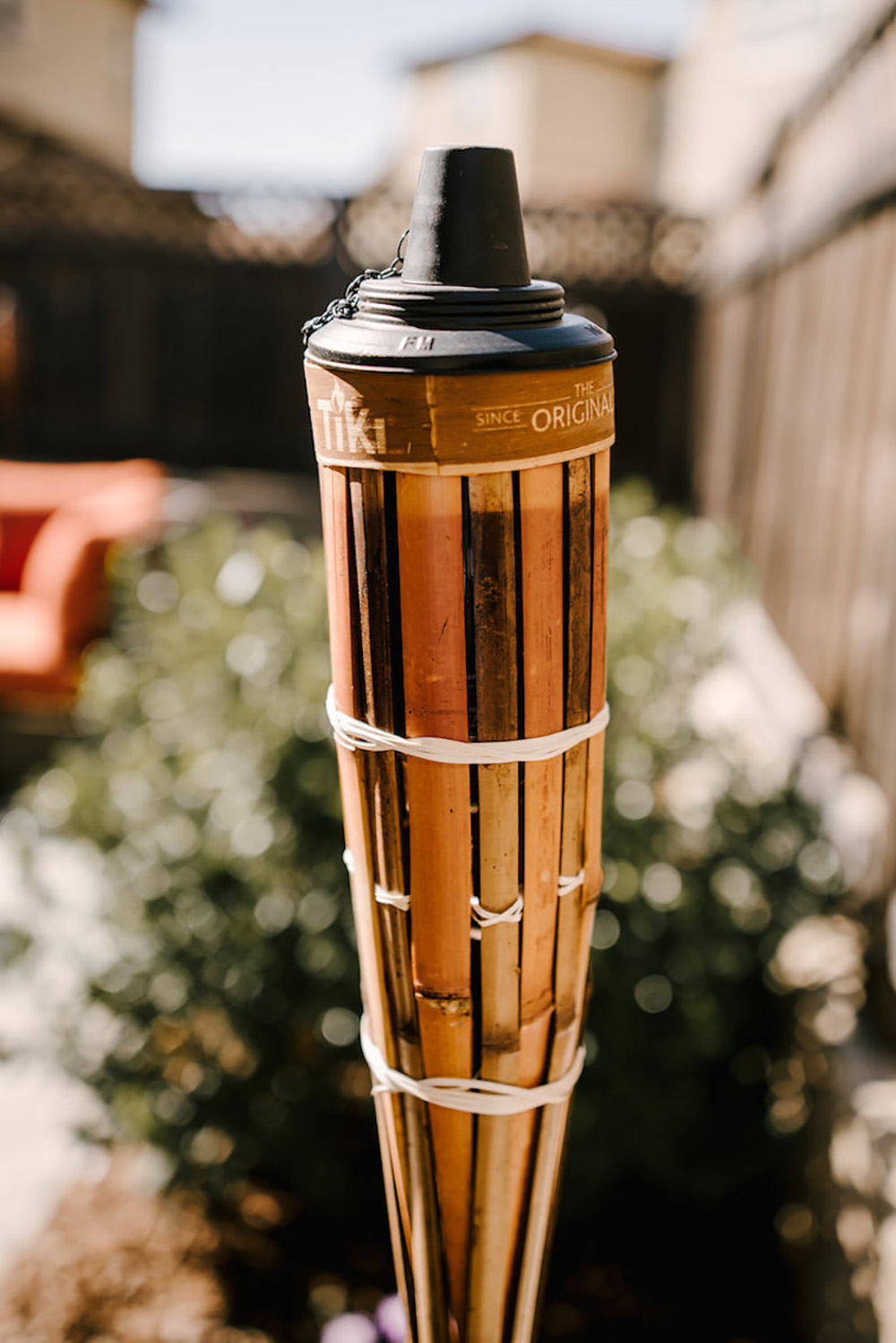 A tiki light with greenery and patio furniture in the background.
