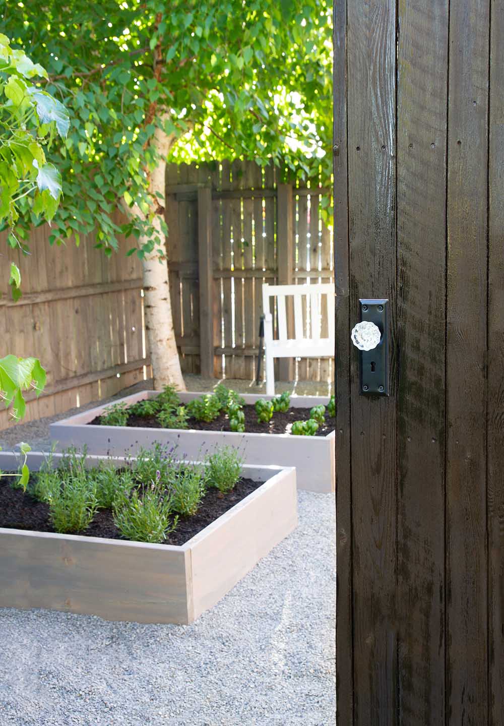 A wooden door opens to a backyard with raised herb garden beds.
