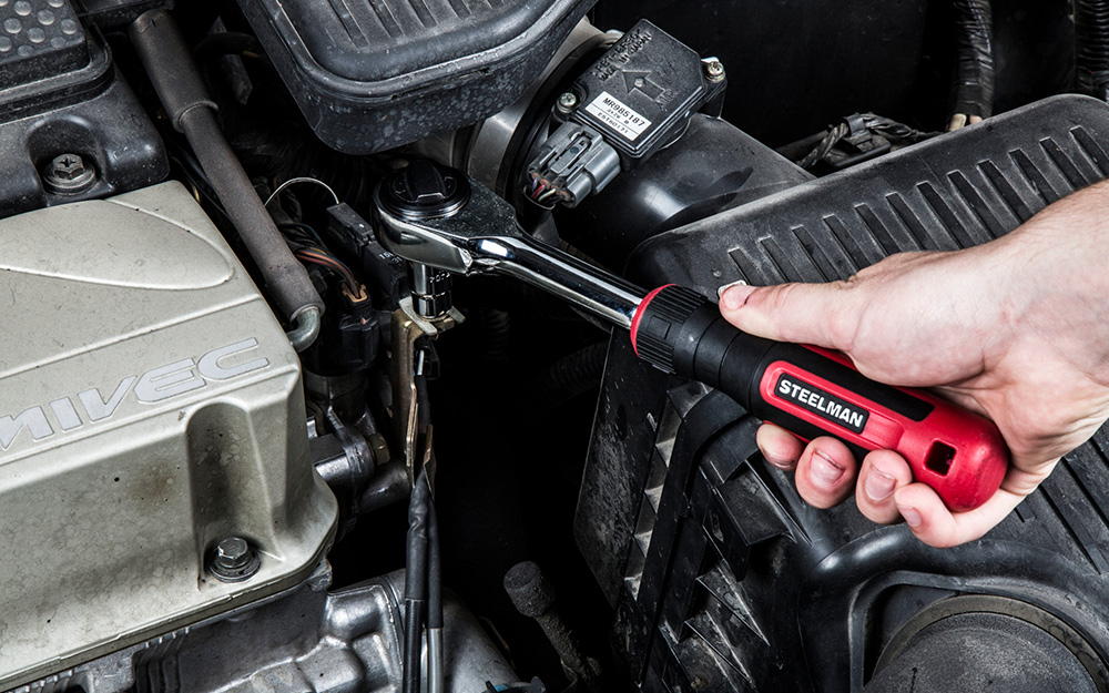 A person uses a ratchet wrench on a car engine.