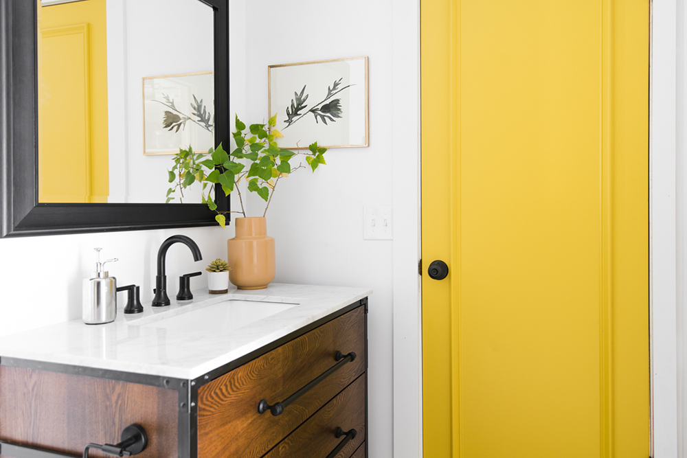 A bright yellow door next to a wooden vanity with black hardware.