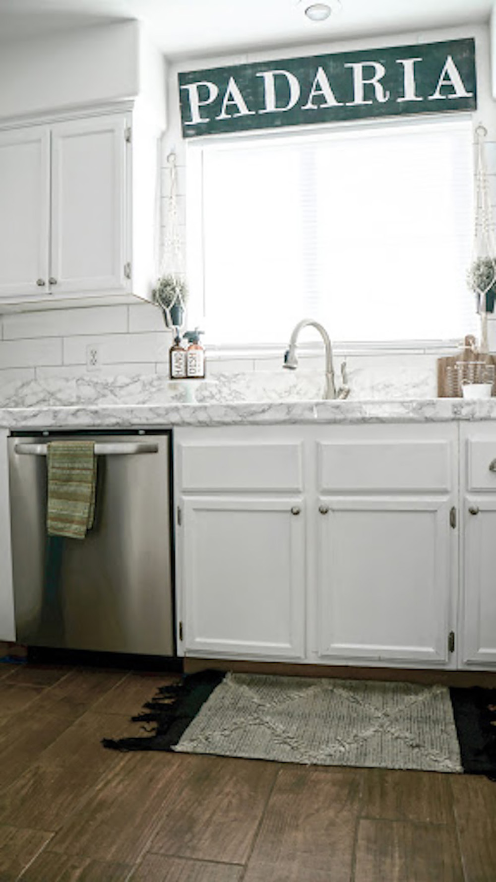 A window sits above a kitchen sink surrounded by white cabinets.