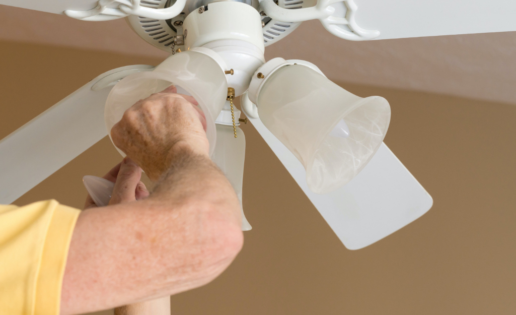 A person changes a lightbulb in a ceiling fan.