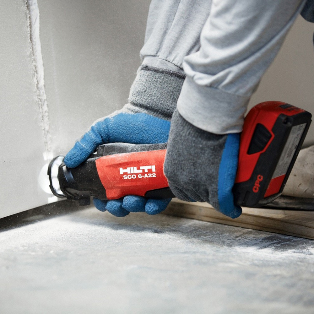 A person uses a rotary tool to sand drywall.