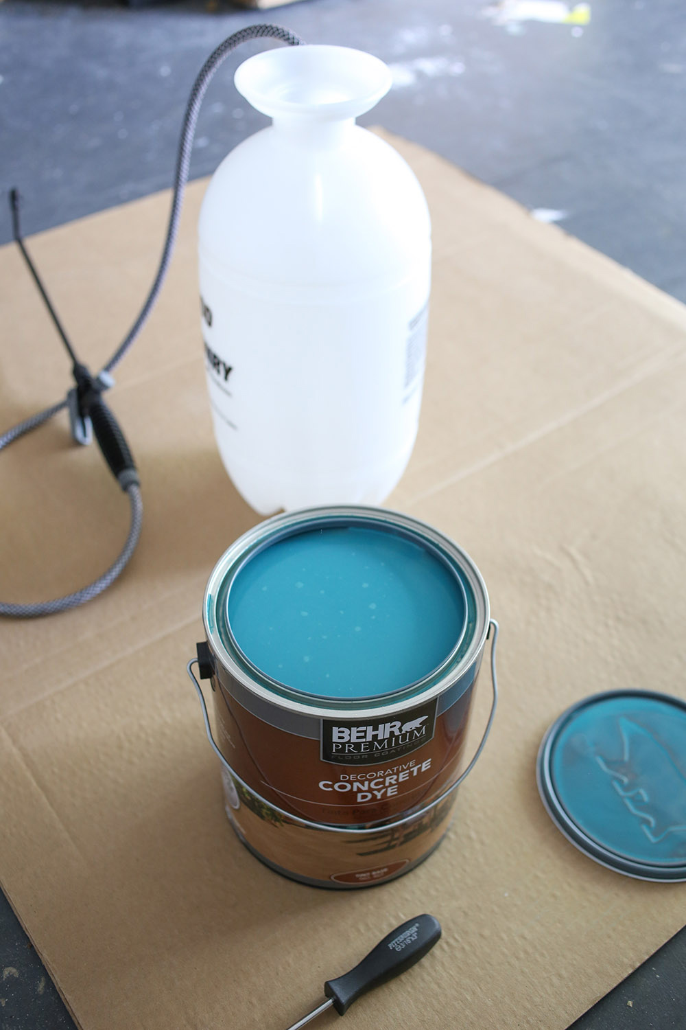 An open can of Behr premium concrete dye and a pump sprayer. An open can of Behr premium concrete dye and a pump sprayer.