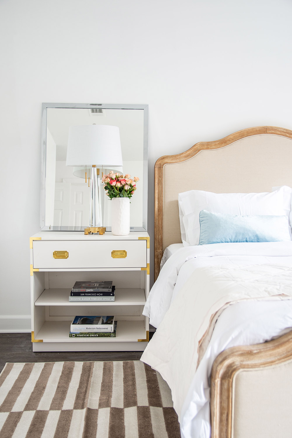 A bedroom scene featuring a bed and nightstand with a lamp and flowers. A bedroom scene featuring a bed and nightstand with a lamp and flowers.