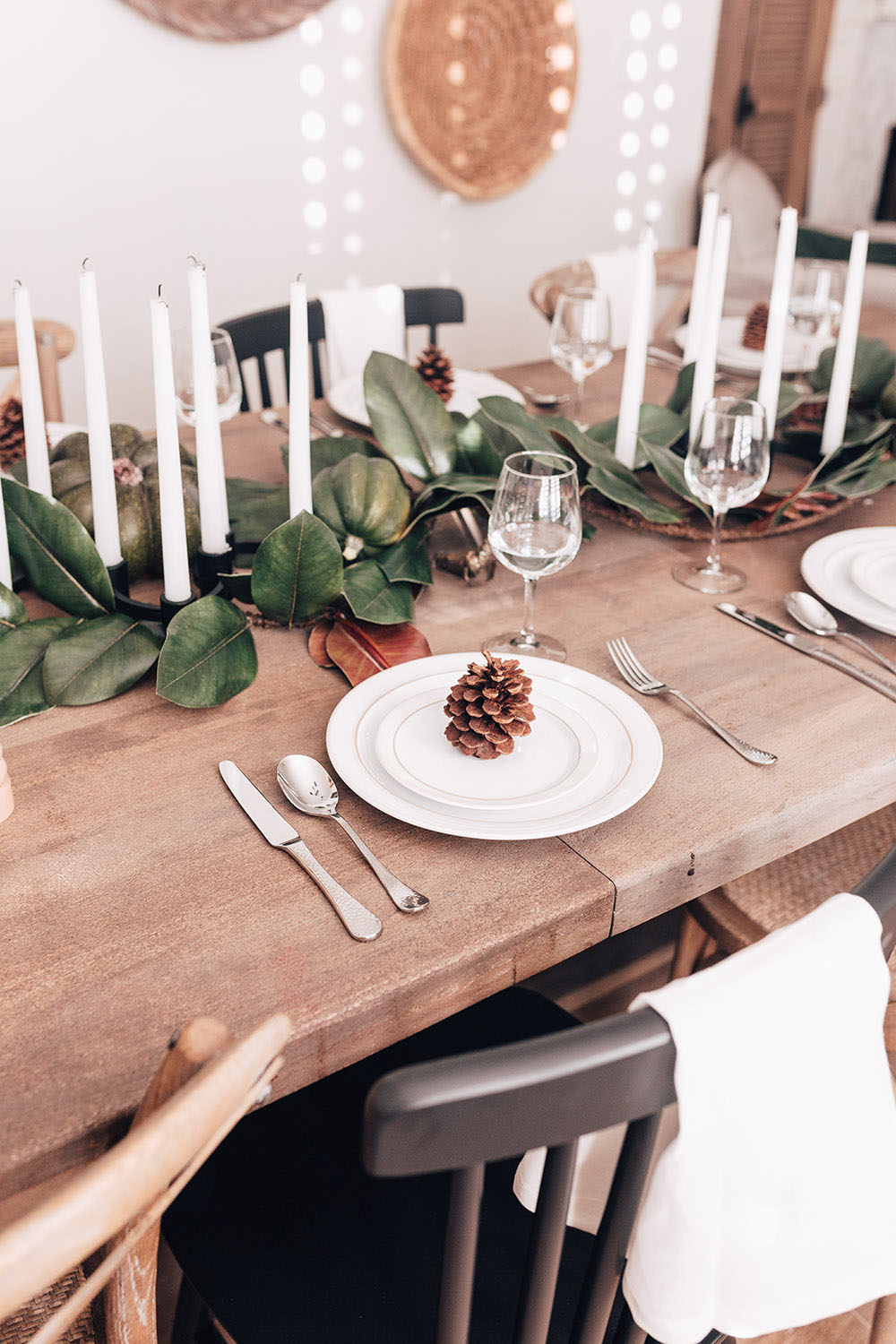 A rustic tablescape featuring white plates, cutlery, glasses, and table decor.