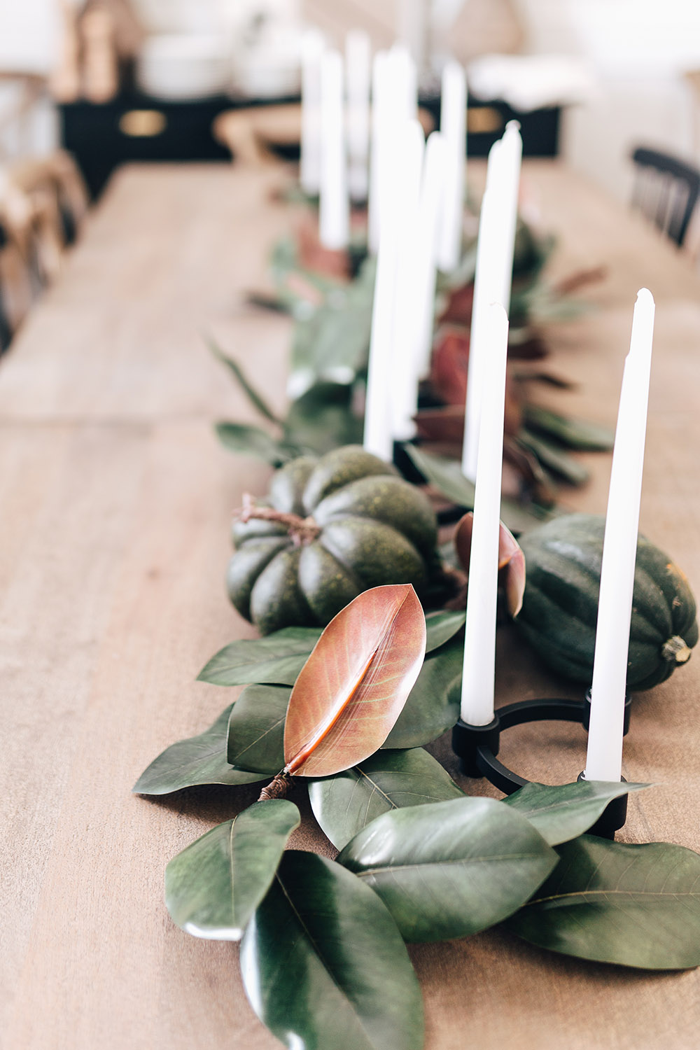A table with white candles, small pumpkins and greenery as the centerpiece. 