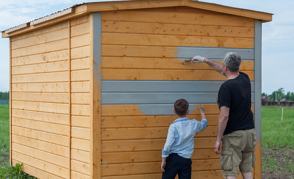 Two people apply a coat of paint to a shed.