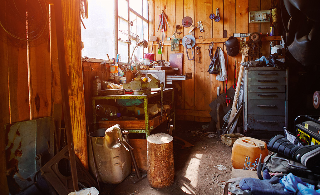 The interior of a cluttered shed filled with yard tools, boots and other clothing.