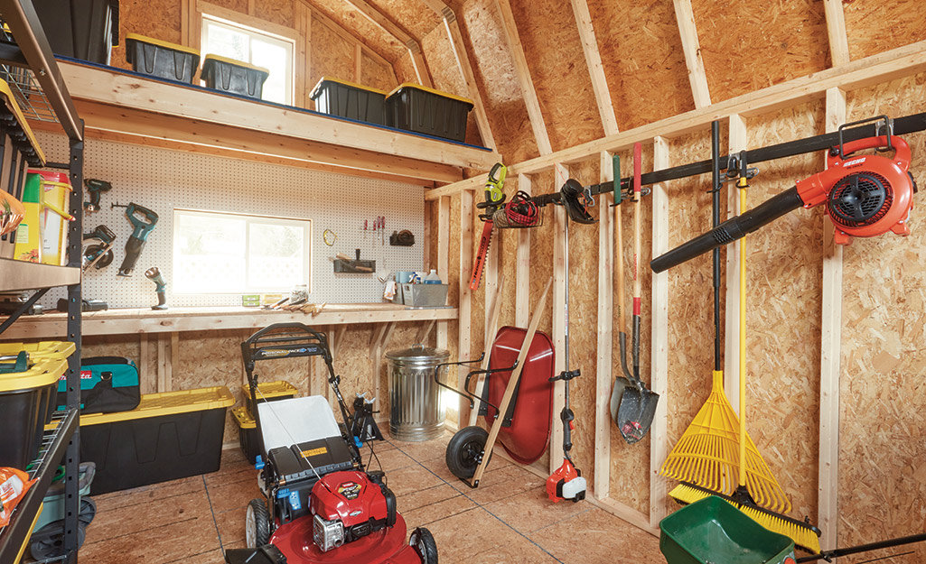 The interior of a shed with a lawn mower and tools hanging from hooks on a wall.