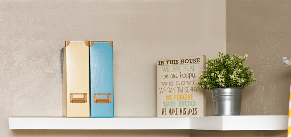 An L-shaped floating shelf holding two magazine storage boxes and small decor items. An L-shaped floating shelf holding two magazine storage boxes and small decor items.