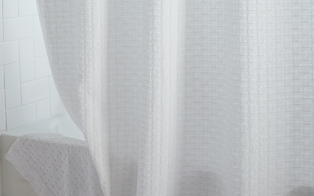 A neutral white shower curtain hanging over a bathtub